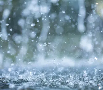 Gouttes de pluie éclaboussant une surface d’eau, capturées en gros plan avec un effet de flou en arrière-plan, illustrant le mouvement dynamique de l’eau.